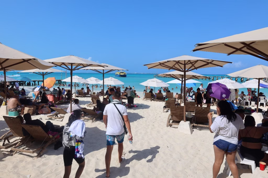 Turistas disfrutan una playa pública de Quintana Roo durante temporada alta. El crecimiento del turismo impulsa la economía estatal, pero también genera presión sobre infraestructura, vivienda y servicios urbanos.