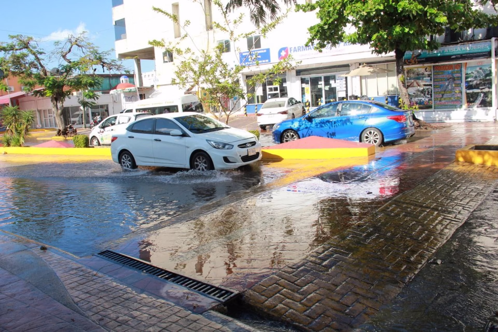 Automóviles circulan junto a un encharcamiento provocado por las lluvias en Quintana Roo.