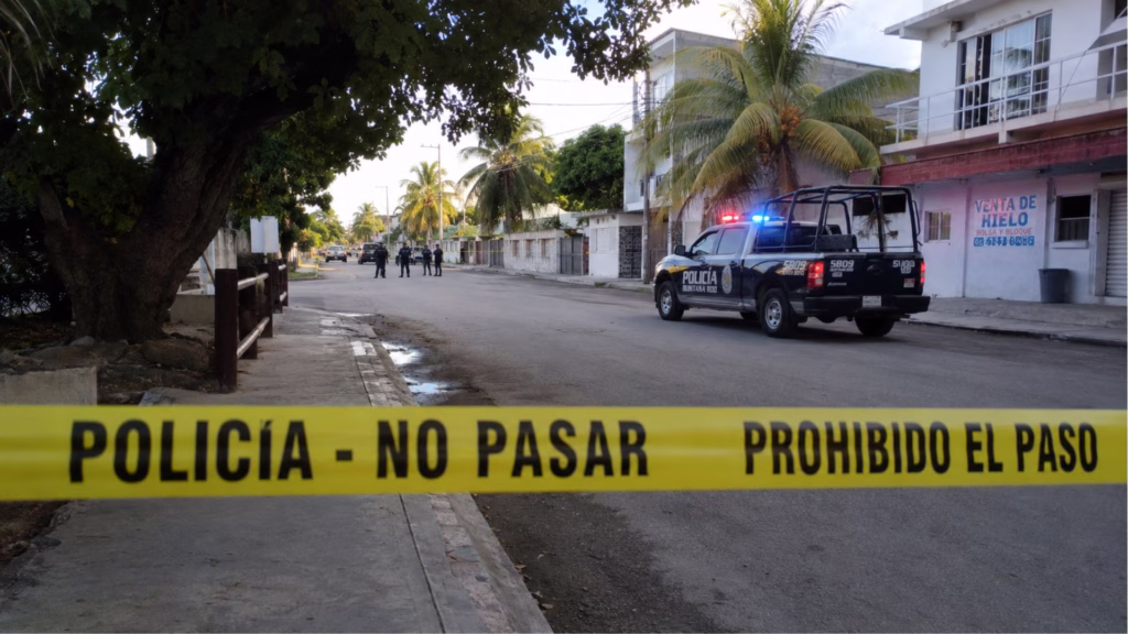 Cinta policial restringe el paso en una calle de Quintana Roo mientras una patrulla y varios agentes permanecen a la distancia.