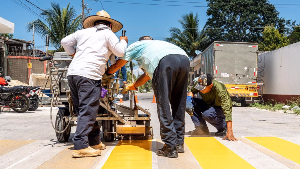 Trabajadores realizan el marcaje de cruces peatonales como parte del programa de seguridad vial en escuelas de Cozumel.