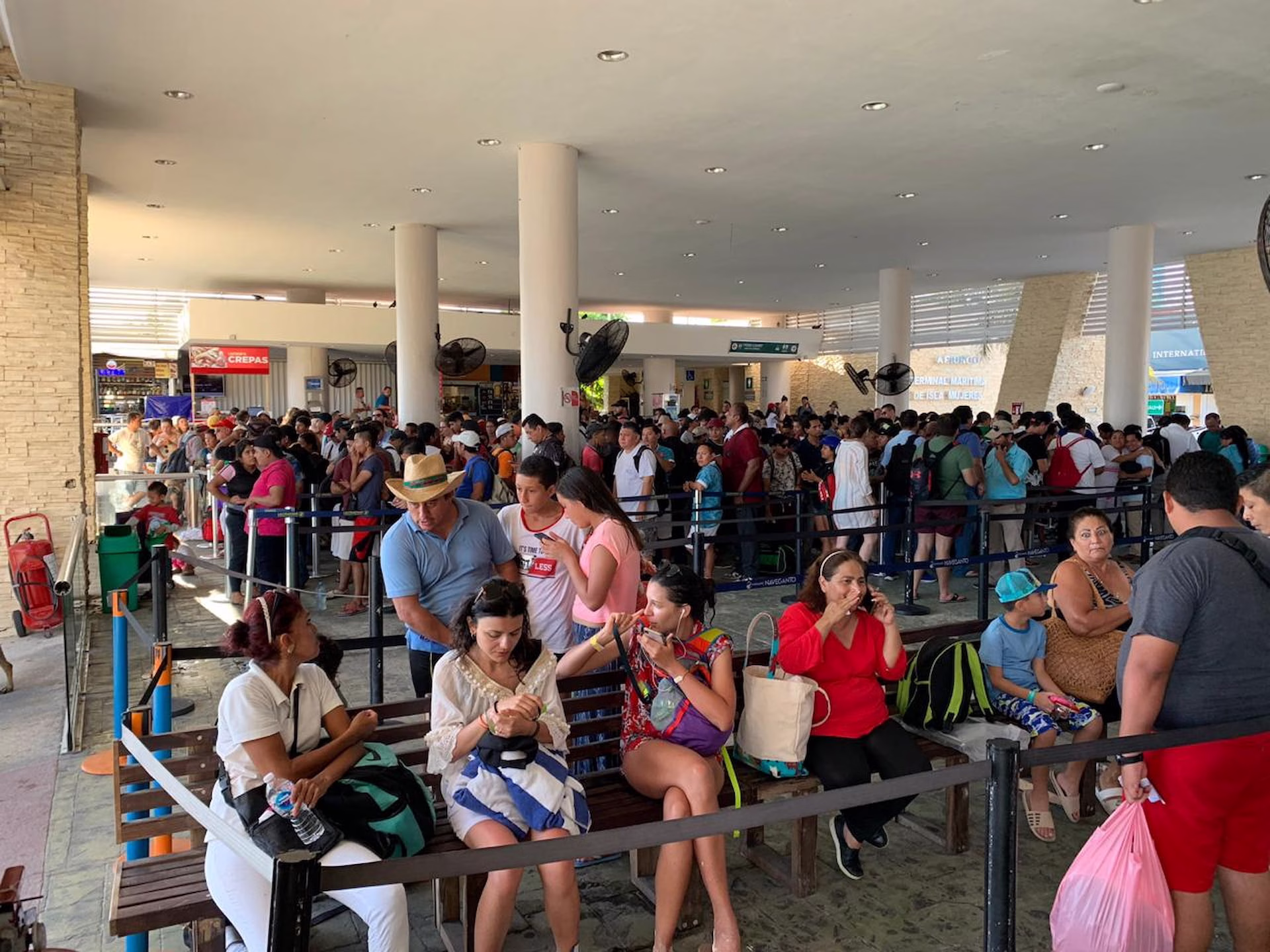 Pasajeros esperan para abordar el ferry a Isla Mujeres en una terminal marítima durante un periodo de alta demanda en vacaciones de verano.