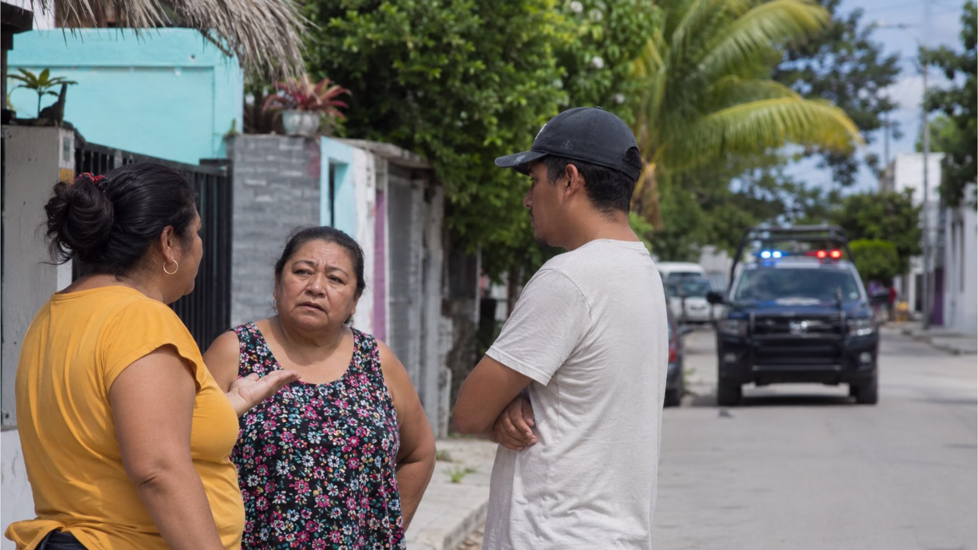 Habitantes conversan en una colonia de Quintana Roo mientras una patrulla permanece al fondo, como referencia a la percepción ciudadana de inseguridad.