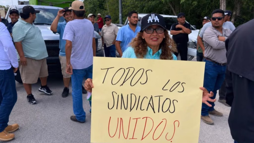 Transportistas en Tulum participan en una protesta pacífica con una pancarta de sindicatos unidos.
