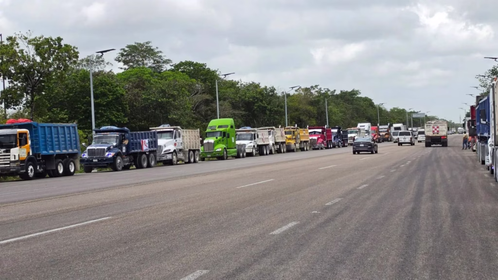 Camiones de carga permanecen formados durante la protesta de transportistas en Tulum sobre la carretera federal 307.