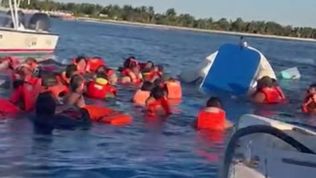 Turistas con chalecos salvavidas permanecen en el mar junto a una embarcación parcialmente hundida durante un rescate náutico.