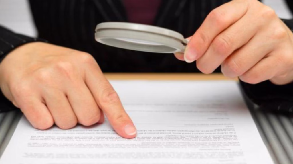 Una persona revisa un documento con una lupa para verificar información contractual.