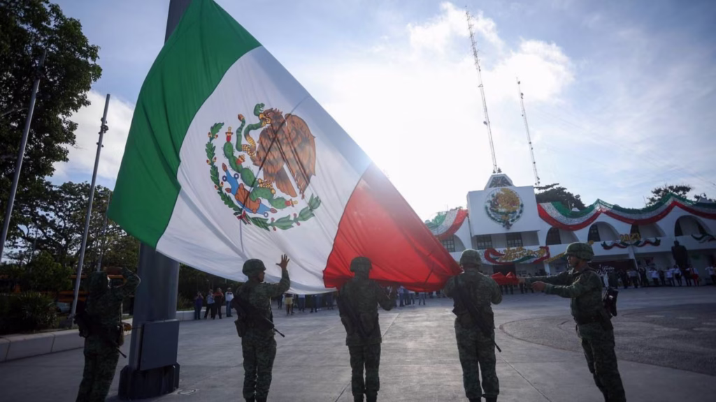 Personal militar despliega una gran Bandera de México frente al Palacio Municipal de Cancún.