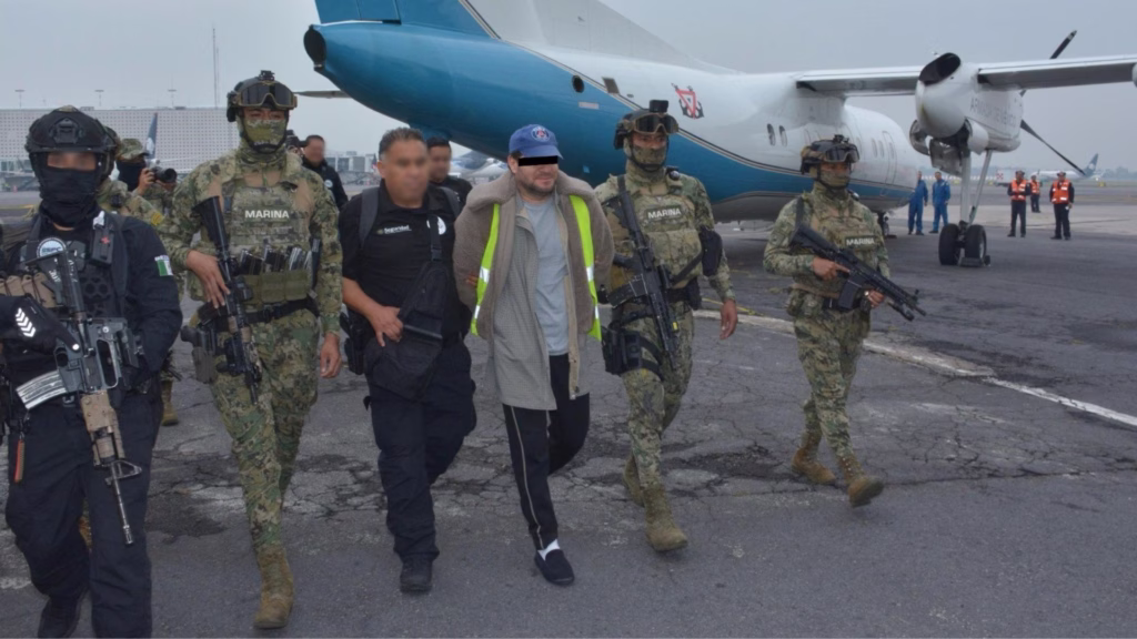 Autoridades trasladan a una persona detenida junto a una aeronave de la Armada de México.