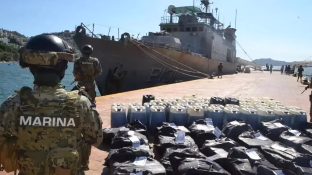 Elementos de la Marina resguardan recipientes y paquetes asegurados junto a una embarcación en un puerto mexicano.